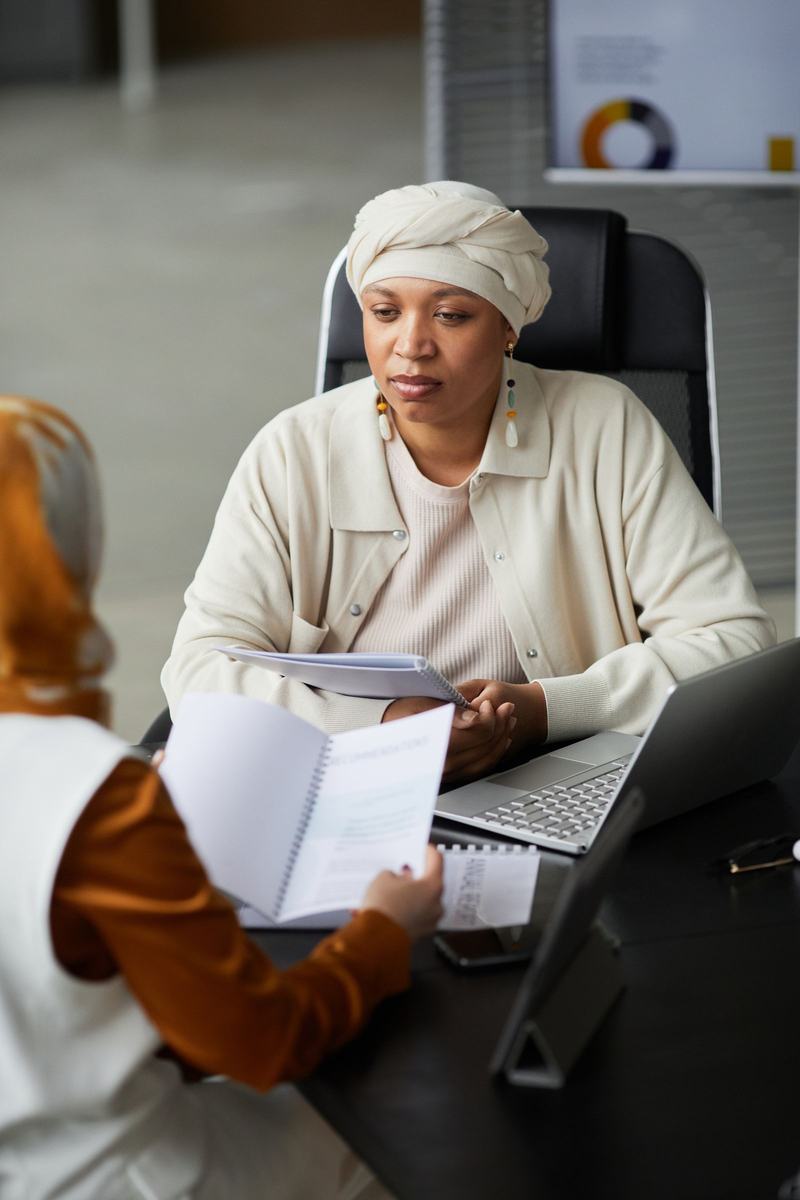 A woman listens closely to the person across the desk from her, holding a few pages of notes